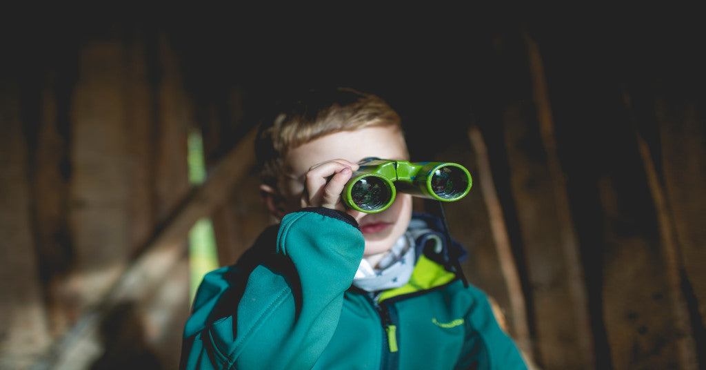Child in blue coat looking through a pair of binoculars