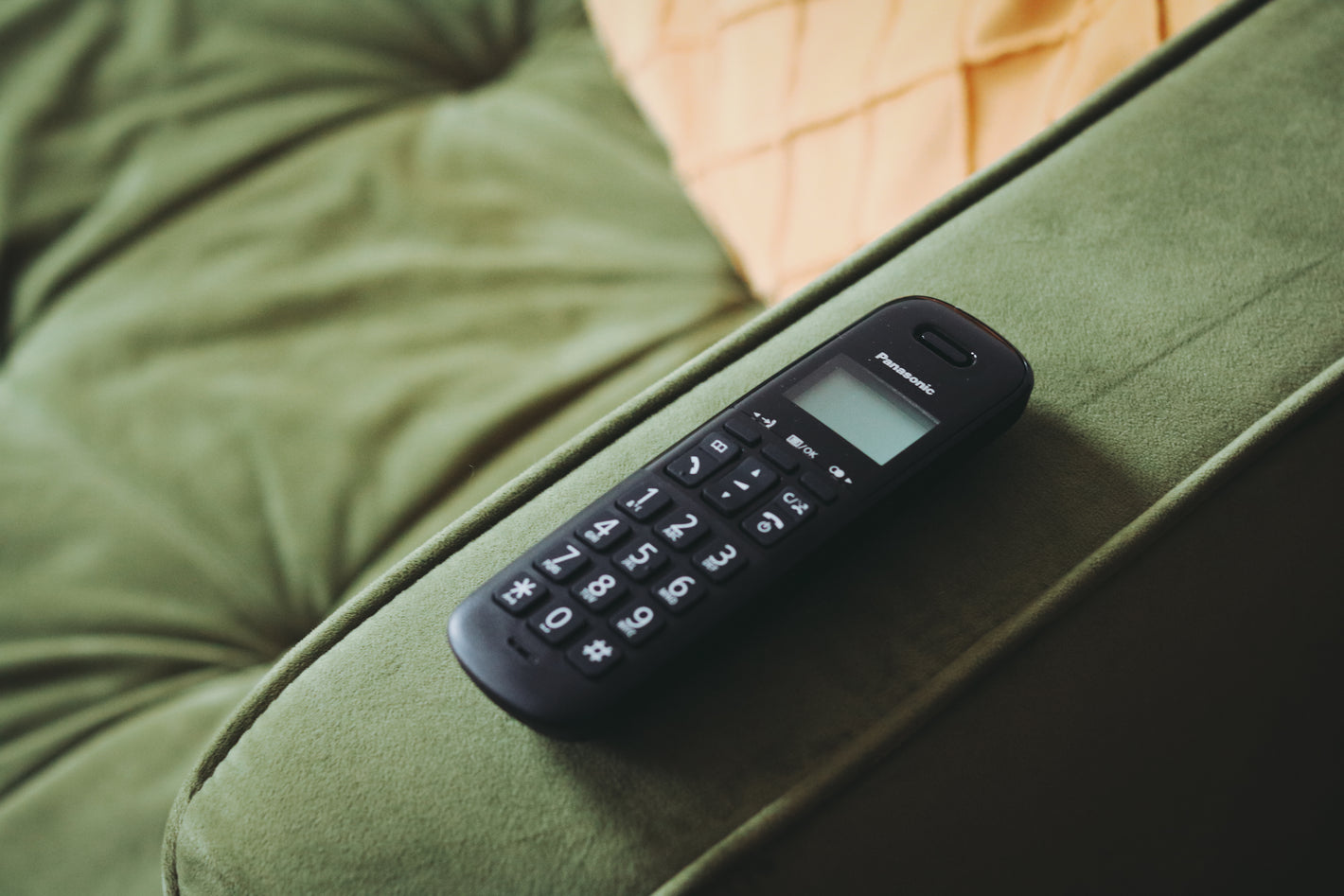 Landline phone handset on arm of green sofa